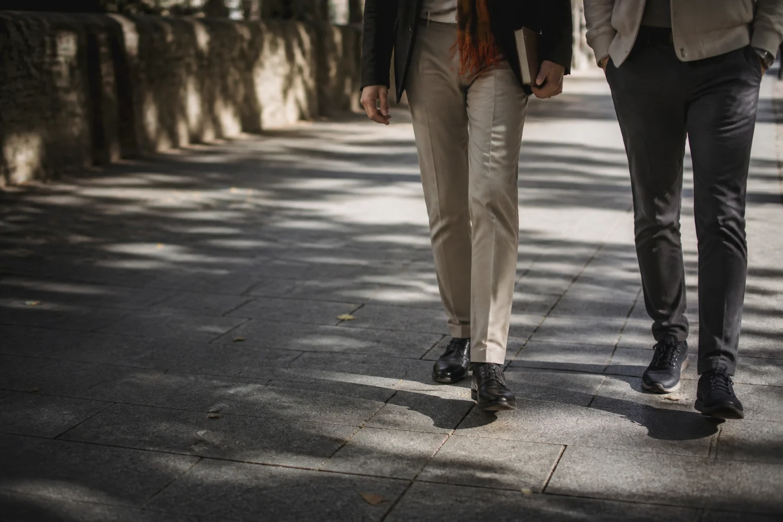 Two adults walking along a shaded city pavement.